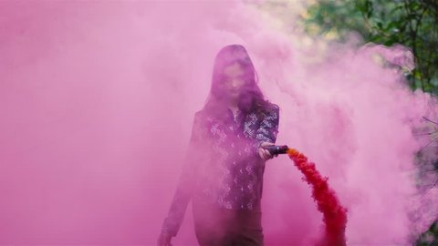 Beautiful girl in a forest waves around a pink smoke grenade and then tosses it behind her, slow motion
