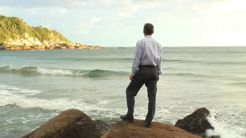HD 1080i: Businessman relaxing while standing on a rock at the sea.