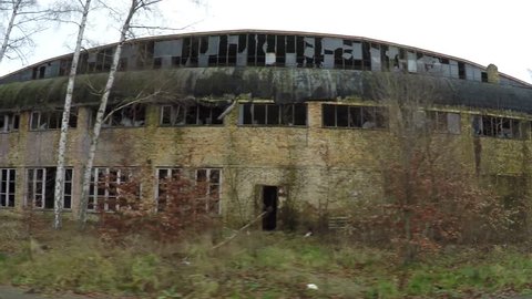 Dolly shot of old abandoned factory ruin showing partly broken windows and old yellow brown stone walls still standing fine and keeping roof steady located in forest yellow grass and some sad trees 4k
