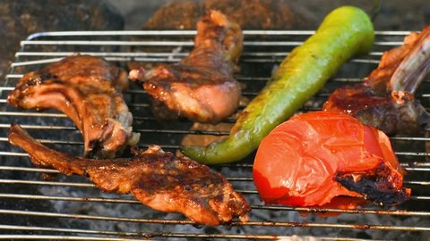 Ribs, green sweet pepper and tomato cooking on the grill over coals