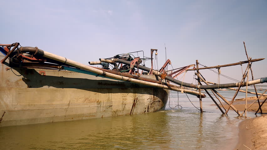 operation of pumping sand out of a dredging boat through a pipe hold between bamboo canes; dredging boat being tied to shore, 