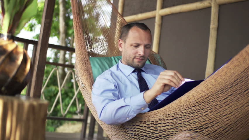 Young businessman working with documents while lying on hammock
