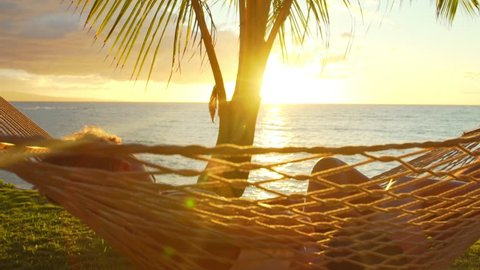 Romantic couple relaxing in tropical hammock at sunset. Summer Luxury Vacation. SLOW MOTION.