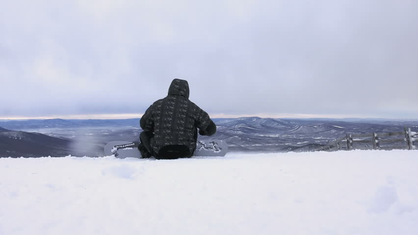 SHEREGESH, RUSSIAN FEDERATION - DECEMBER 7, 2015: Man is preparing his equipment to snowboarding on mountain top and then snow closes up the camera lens