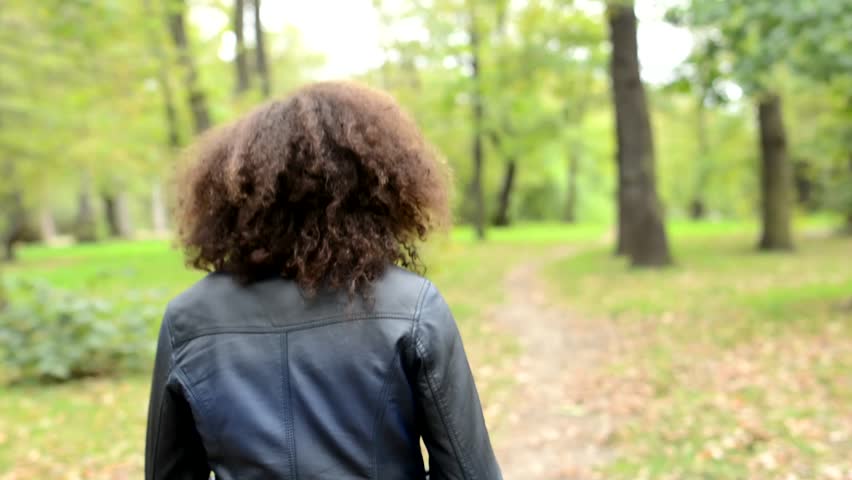 young charming african girl walks in the forest and observe the landscape - camera focus her back then face