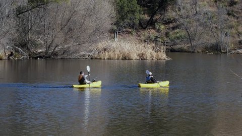 Two men paddling kayaks on a calm mountain lake