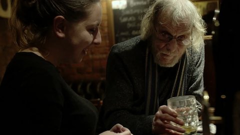 old man drinking beer and talking with a young woman in a pub