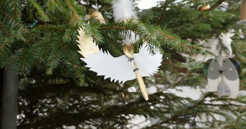 Tilt-up to hand-made traditional Christmas angel ornament made from teaspoon and paper and capsules, plastic and sugar, painted by kids on a fir tree in the city of Thann, Alsace, France