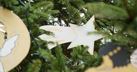 Zoom out from hand-made traditional Christmas ornament - angel cupidon on trumpet, angel on moon, star made from paper and painted by kids on a fir tree in the city of Thann, Alsace, France