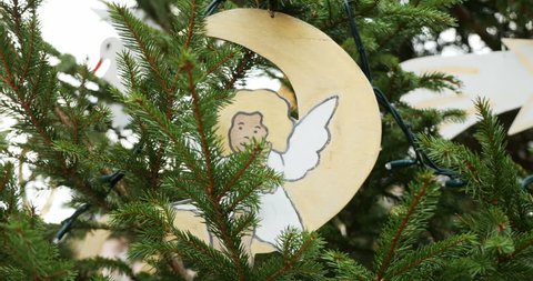 Zoom out from hand-made traditional Christmas ornament - angel on moon, from paper and painted by kids on a fir tree in the city of Thann, Alsace, France