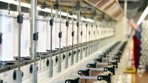 Textile Industry. Row of automated machines for yarn manufacturing. 
Yarn thread running in the machine. Worker on the production line in a textile mill.