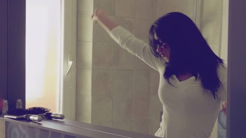 Happy woman dancing in bathroom while brushing long black hair closeup