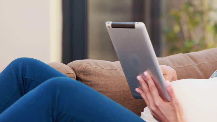 Pregnant Caucasian woman lying on the couch while using tablet at home