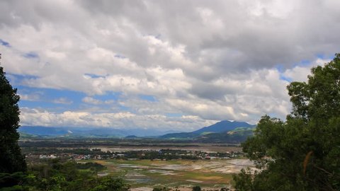 upper panorama of distant rice fields in water and village against mountains and green trees at foreground