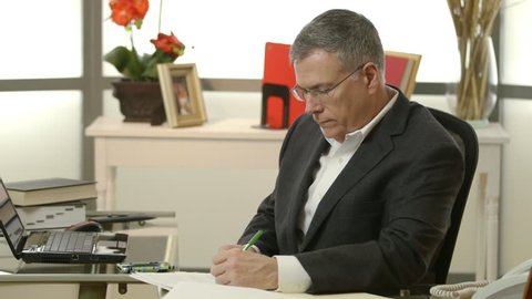A mature CEO in his office stops working then removes reading glasses and smiles