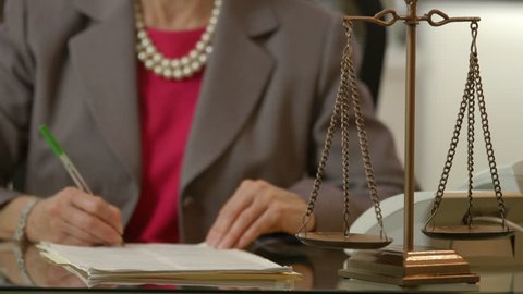 Focus is on the scales of justice with a female attorney out of focus working in the background.