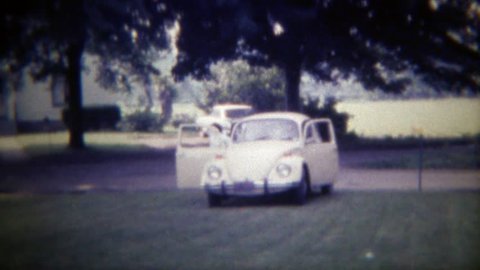 DES MOINES, IOWA 1971: Family arrives in Volkswagen Beetle Bug car parks on lawn.