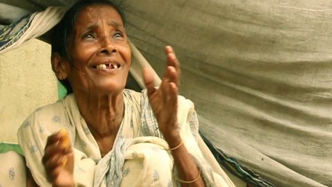 Elderly Indian woman smiles and fold hands in gratitude upon receiving some vegetarian food. She has been put out of home by a big flood