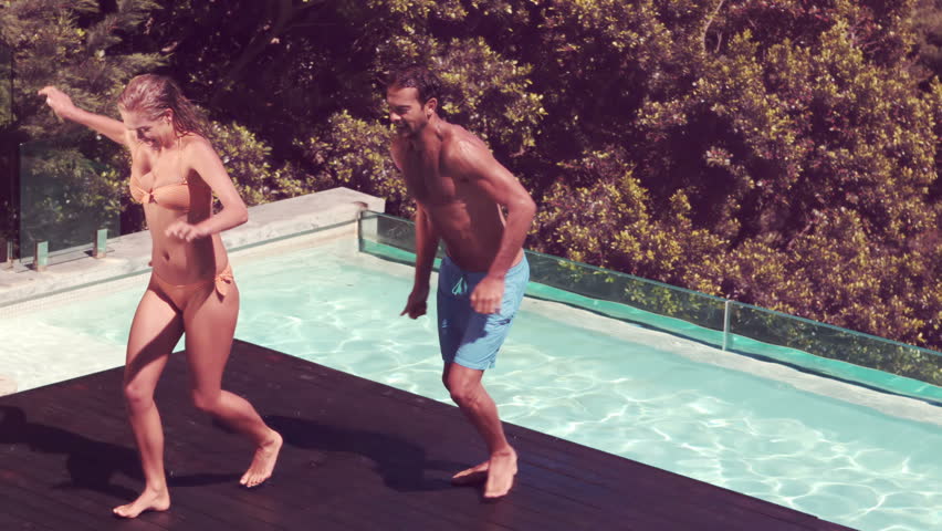 Couple jumping into swimming pool making huge splash in slow motion