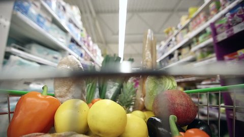 Full shopping cart with healthy food moving through aisles of supermarket. Time lapse