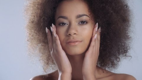 Portrait of a sensual young African woman posing against a white background. Pretty girl with afro hair touching her face. Beauty and skincare concept. 