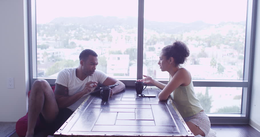 4k Black and Hispanic couple talking and using phone and tablet computer in living room