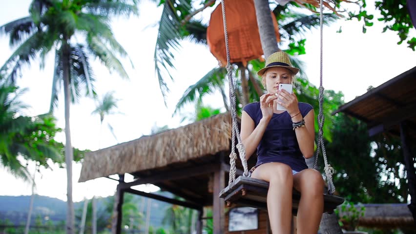 A young woman using the phone sitting on a swing
