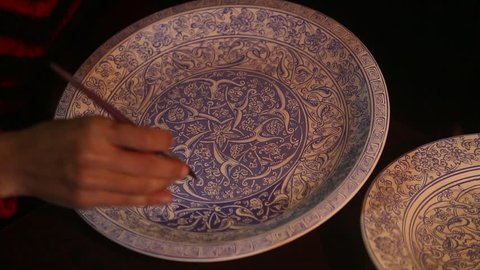 IZNIK, BURSA, TURKEY - MARCH 2015: Woman paints tile on ceramic plates.Iznik pottery, named after the town in western Anatolia, was produced between last quarter of the 15th century, 17th century. 