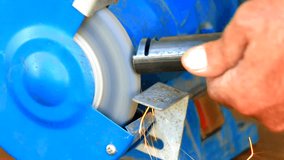 Worker grinding metal component on bench grinder closeup
