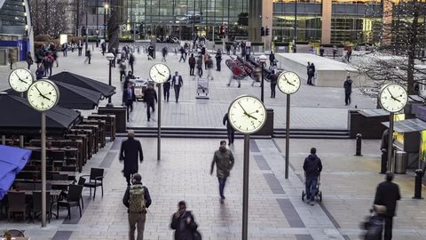 Timelapse of people rushing from work with several clocks in the docklands financial centre in London