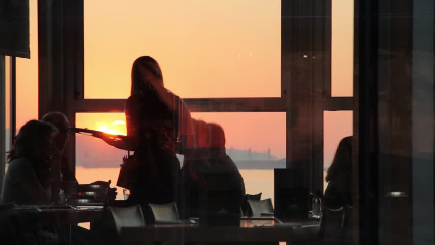 A restaurant waitress serving clients with a golden sunset as the backdrop.