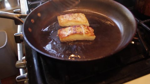 white fish fillets cooking on stove, flipped with spatulas