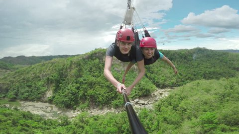 Great footage of a happy couple sliding down a zip line in tandem, over a canyon and into the woods. Part two, filmed of a selfiestick.