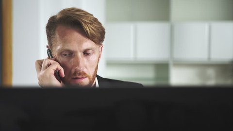 Red-haired man sitting at a computer and calling on the phone
