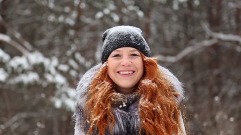 Beauty young woman with red long hair enjoying winter day outside. Redhead Christmas girl spinning around while throwing snow up laughing and smiling happily at winter trees background. Slow motion