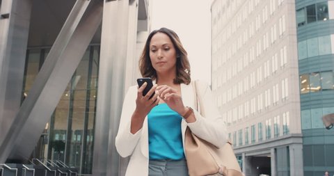 Beautiful mixed race business woman walking through city connected using smart phone