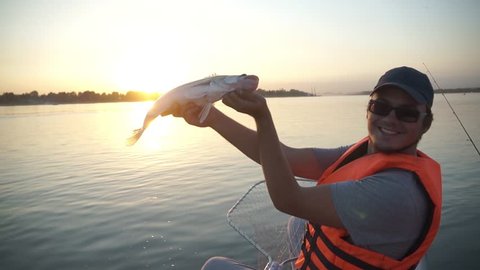 fisherman man holding a big fish pike. sunset