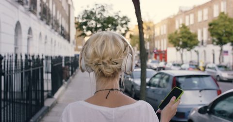Happy Beautiful blonde listening to music on smart phone walking in the city