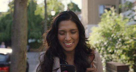 Beautiful Indian woman walking through city living happy lifestyle using smart phone reading social media วิดีโอสต็อก