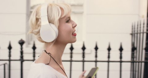 Happy Beautiful blonde listening to music on smart phone walking in the city స్టాక్ వీడియో