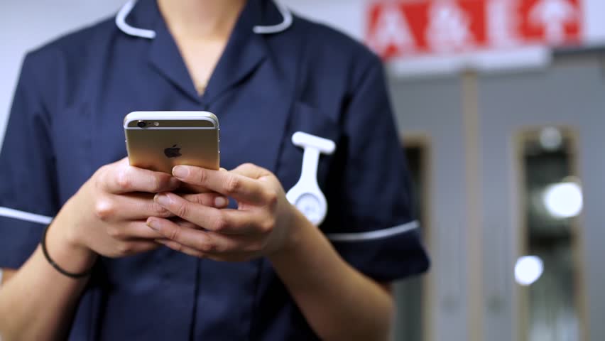 Nurse using cellular mobile phone in front of doors in hospital
