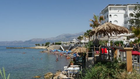 LIMENAS HERSONISSOU, CRETE, GREECE - JUNE 17, 2015: A straw umbrella shades cafe tables along the Aegean shore in the resort town of Limenas Hersonissou.