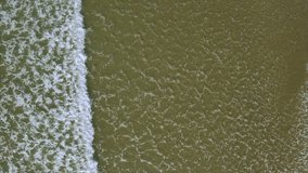 Aerial drone video of waves splashing on shore. Tracking shot of water creating texture from white foam. Slow motion of waves changing patterns. The footage is filmed from an overhead perspective.