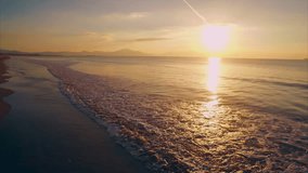 Scenic drone footage of waves reaching beach during sunset. Slow motion tilt up shot of beautiful sea and sun. Reflection of sunlight is falling in seascape