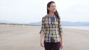Slow motion video of beautiful woman walking on beach. Attractive female is in casual wear. Tracking shot of smiling woman enjoying nature.