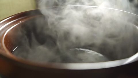 Steaming water in brown pot, slow motion video