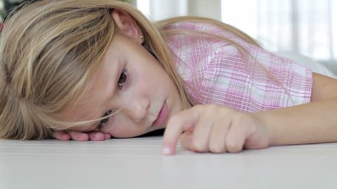 Portrait of sad little girl lying on floor at home at the day time