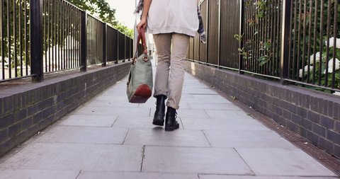 Detail of woman's feet walking through city on pavement from behind carrying handbag