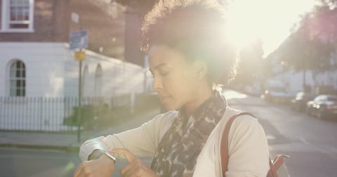 Beautiful Mixed race woman using smart watch technology app walking through city streets living urban happy lifestyle