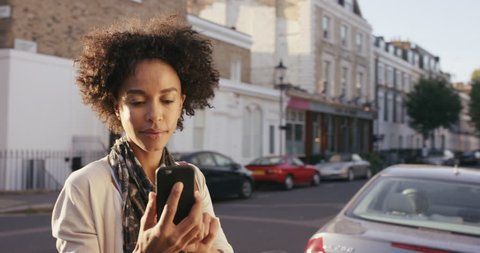 Beautiful Mixed race woman using smart phone technology app walking through city streets living urban happy lifestyle
